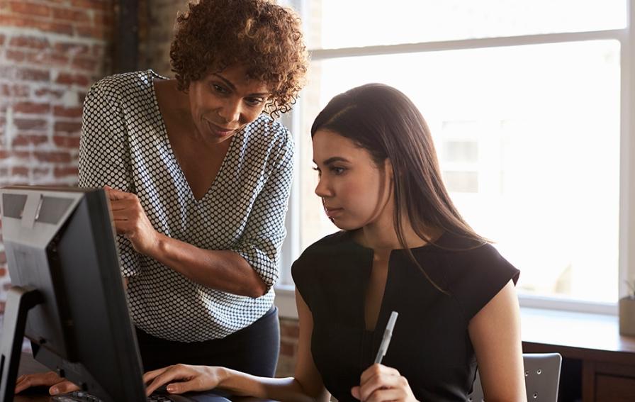 A professional businesswoman shows a business student a process on a desktop computer